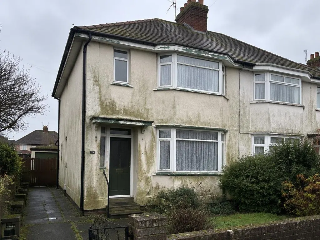 Semi-detached house with stained, mossy cream render and a dark green front door