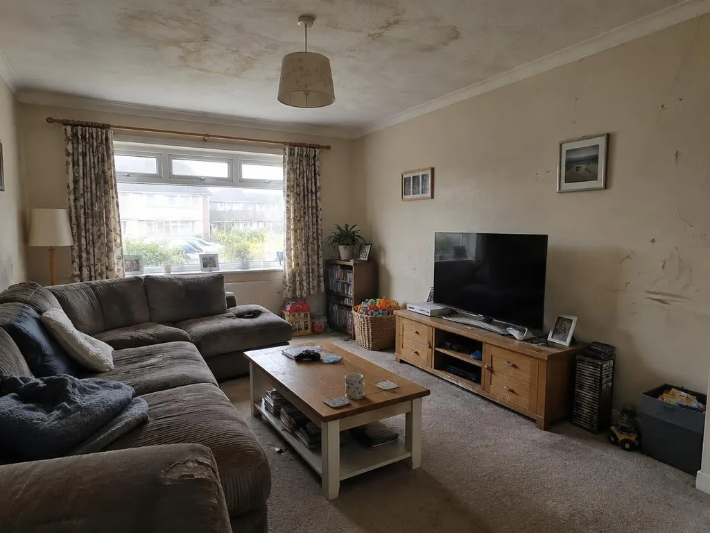 Living room with stained ceiling, marked cream walls, a corner sofa and a TV unit